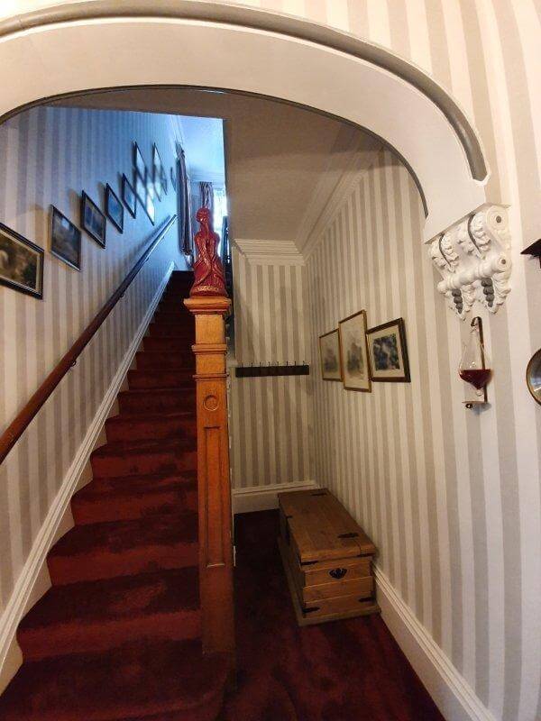 A traditional hallway and stairs with striped wallpaper and bold red carpet