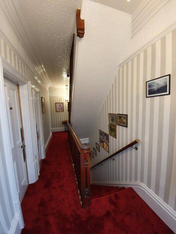 A traditional landing and stairs with striped wallpaper and bold red carpet