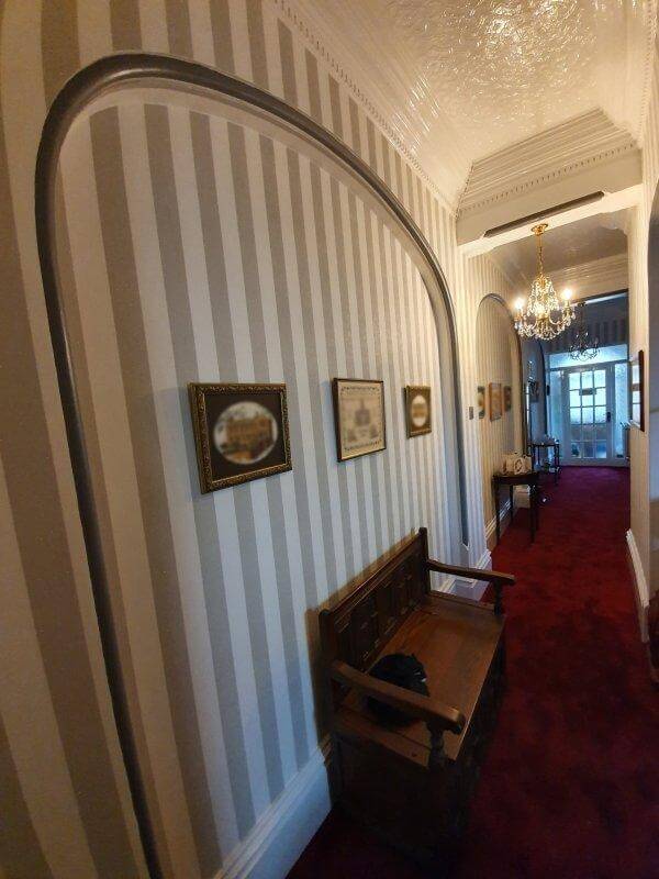 A traditional hallway with striped wallpaper and bold red carpet